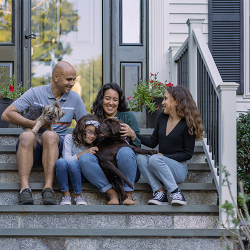 Happy family of four sitting on steps with dog.