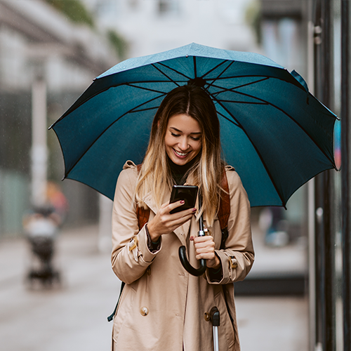 Smiling woman holding umbrella and mobile device.